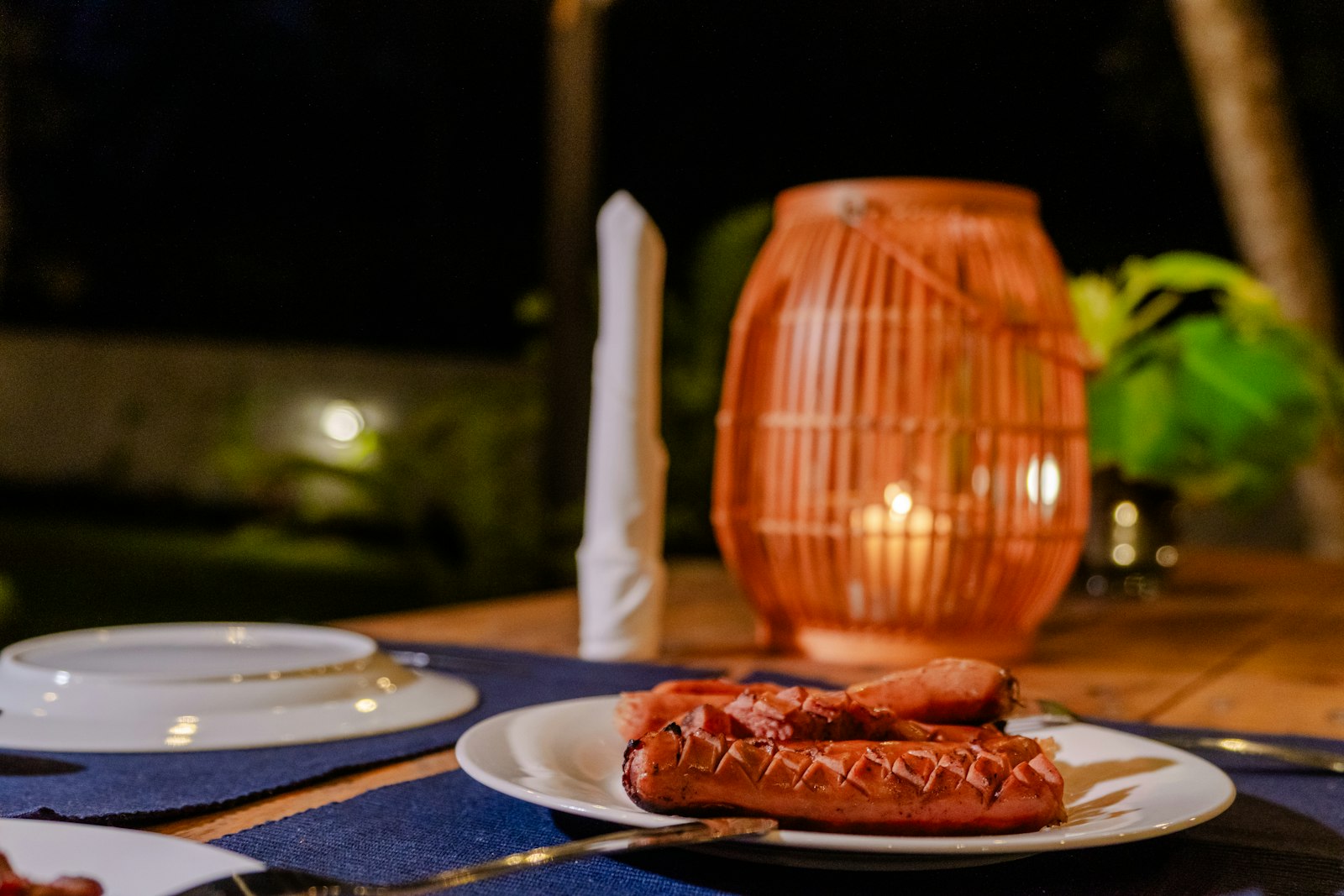 Outdoor villa BBQ at night — grilled meats, lantern, candlelit table
