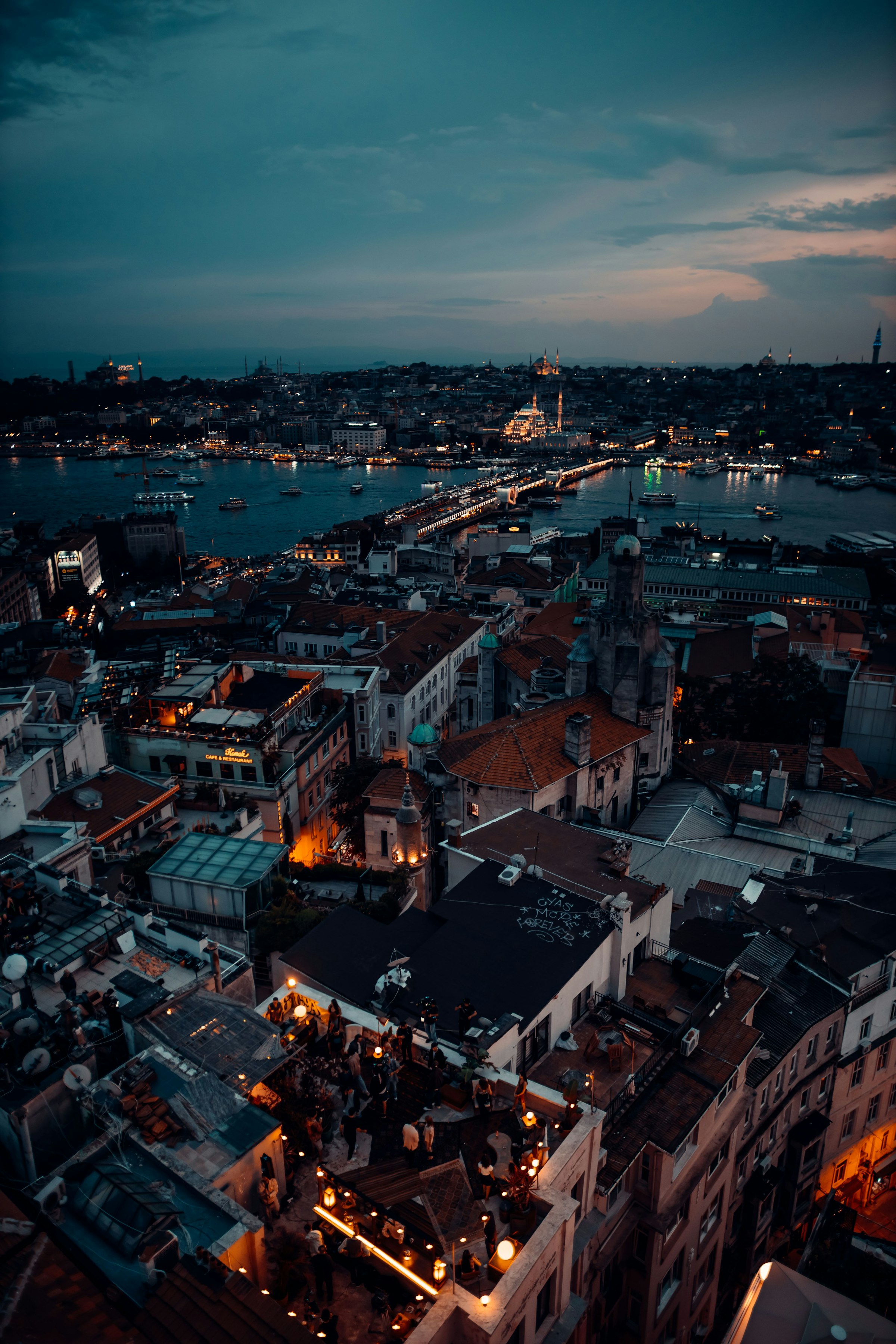 Istanbul rooftops at blue hour viewed from Galata — the Golden Horn, mosque silhouettes, and rooftop lights